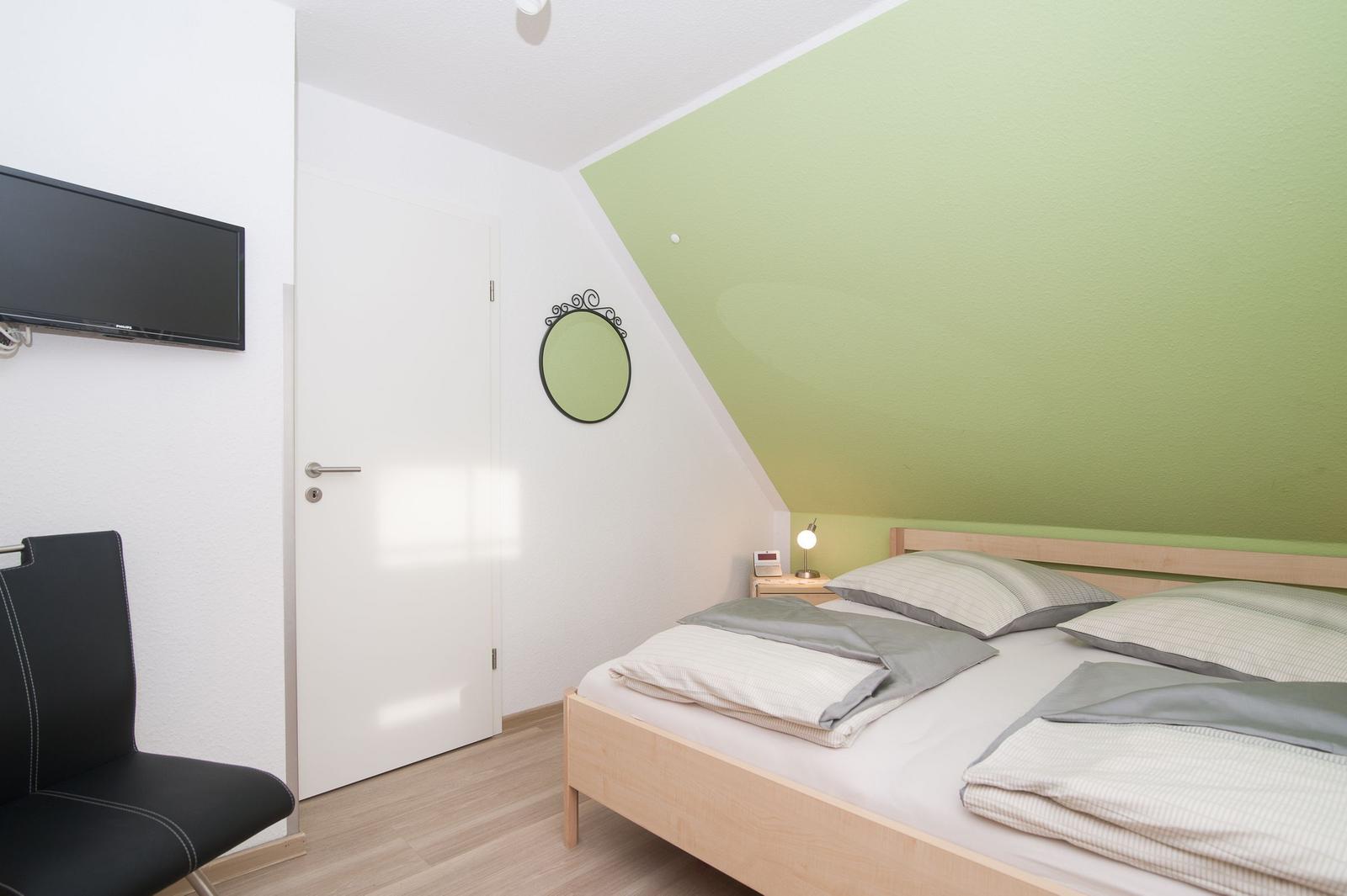 Schlafzimmer mit Bett, Fernseher und grüner Wand