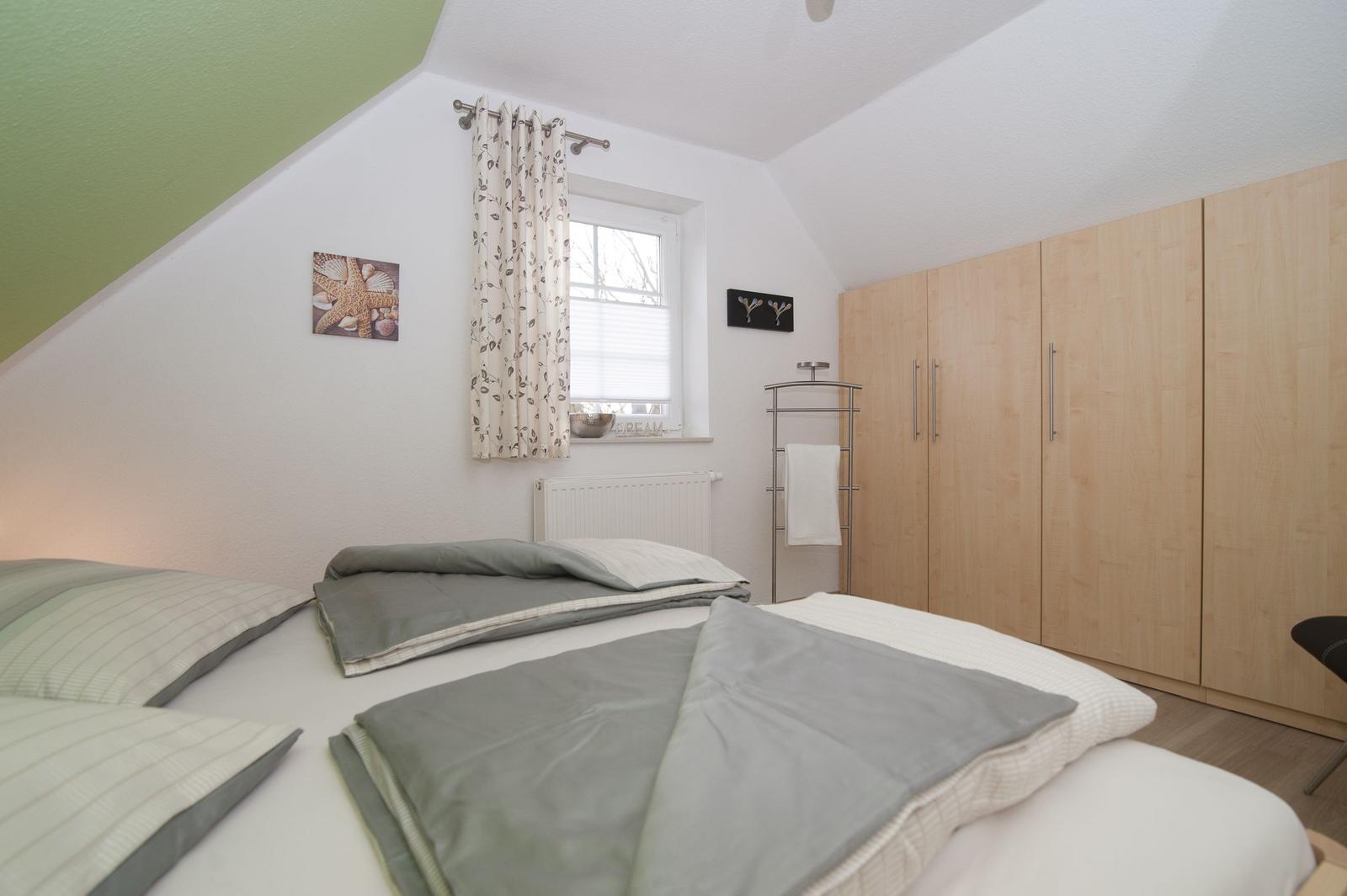 Schlafzimmer mit Doppelbett, Kleiderschrank und Fenster mit Vorhängen.