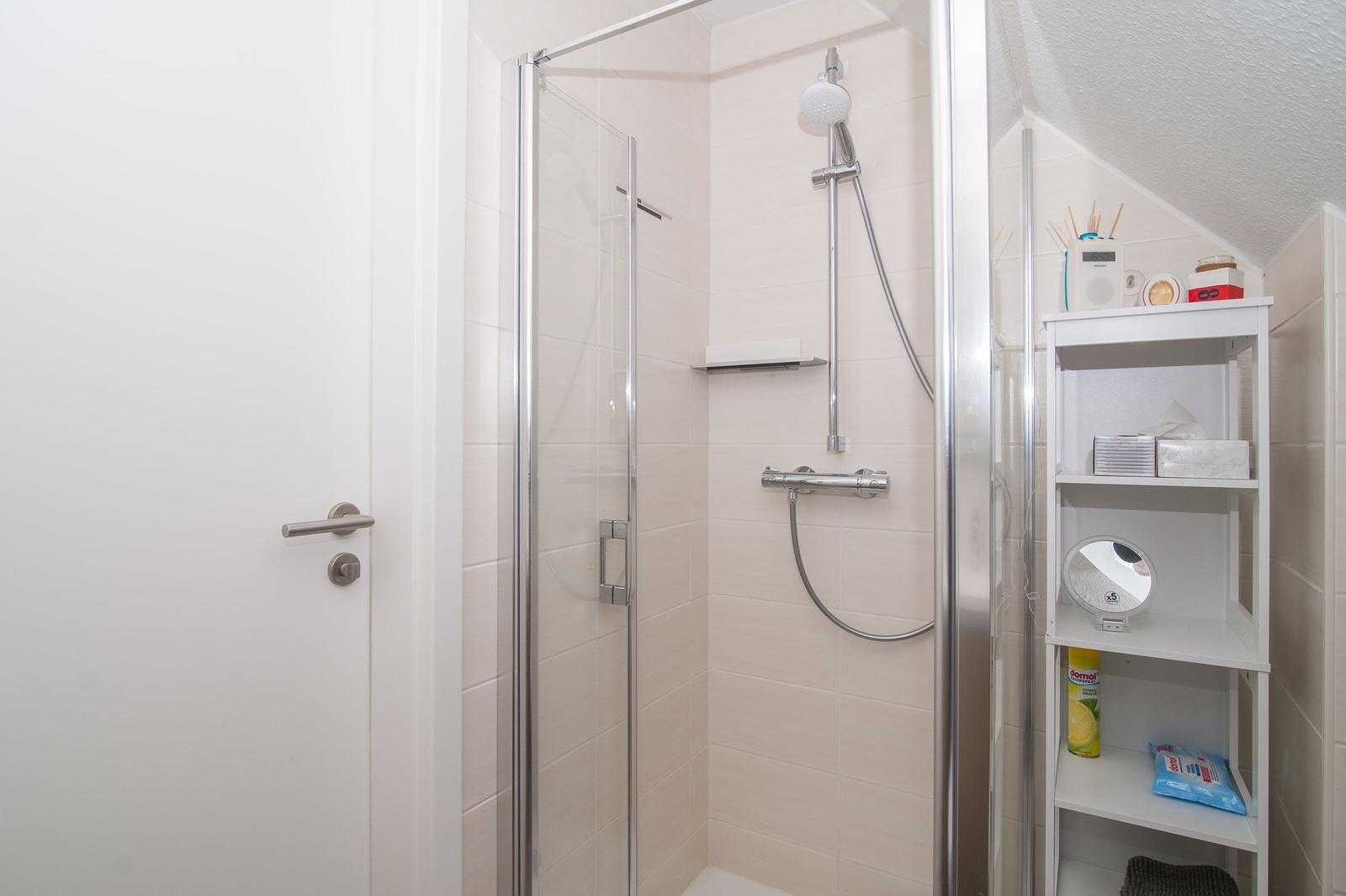 Dusche mit Glaswand, Duschbrause und Regal mit Badartikeln