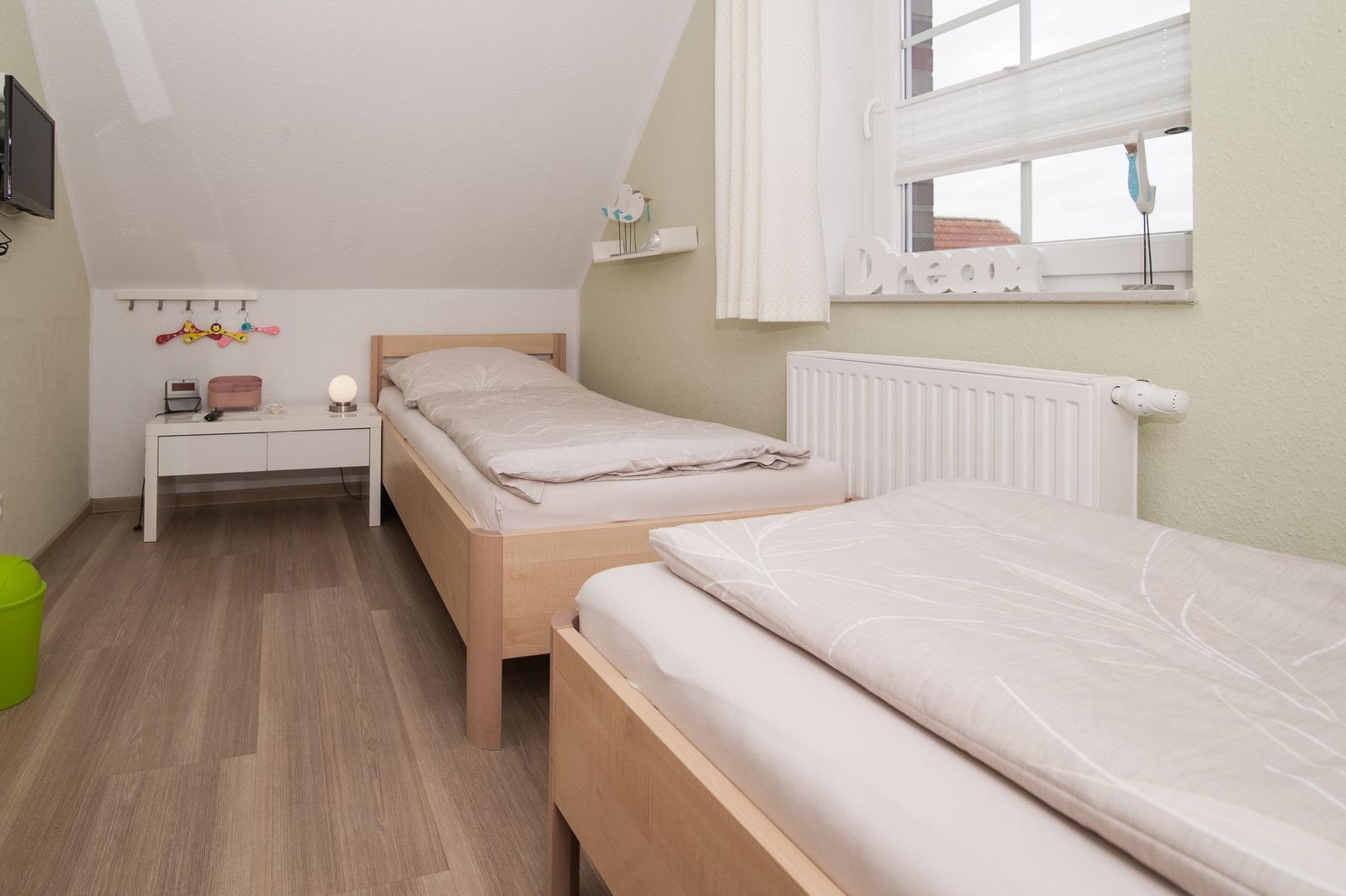 Zwei Einzelbetten, Schreibtisch und Fenster mit Vorhang.