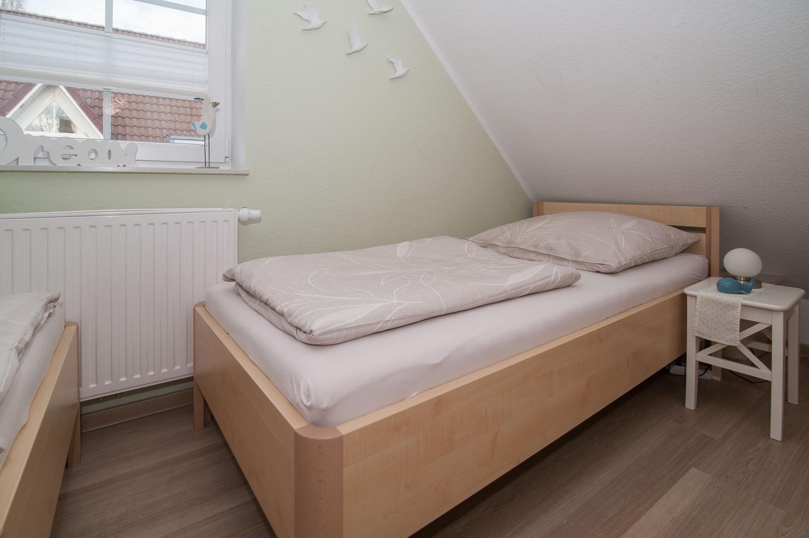 Ein Schlafzimmer mit Dachschrägen, einem Bett, Nachttisch und Fenster.