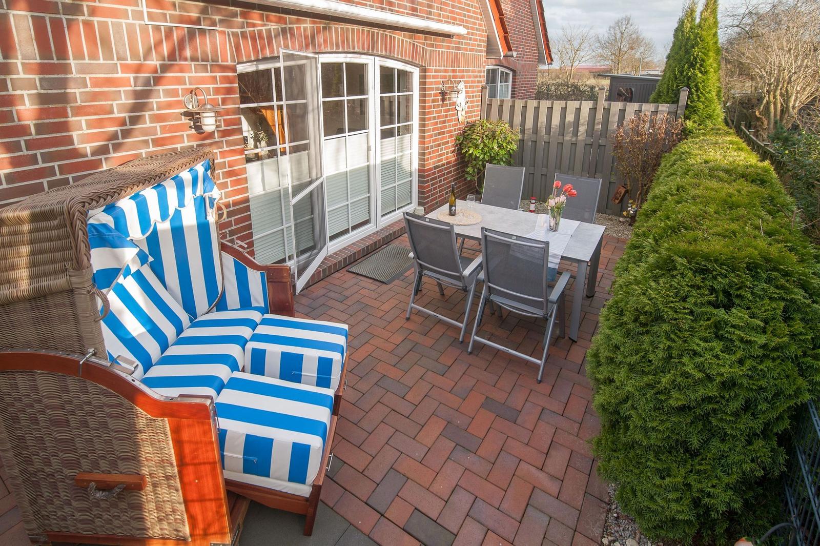 Terrasse mit blau-weißem Sofa, Tisch und Stühlen neben Backsteinhaus.