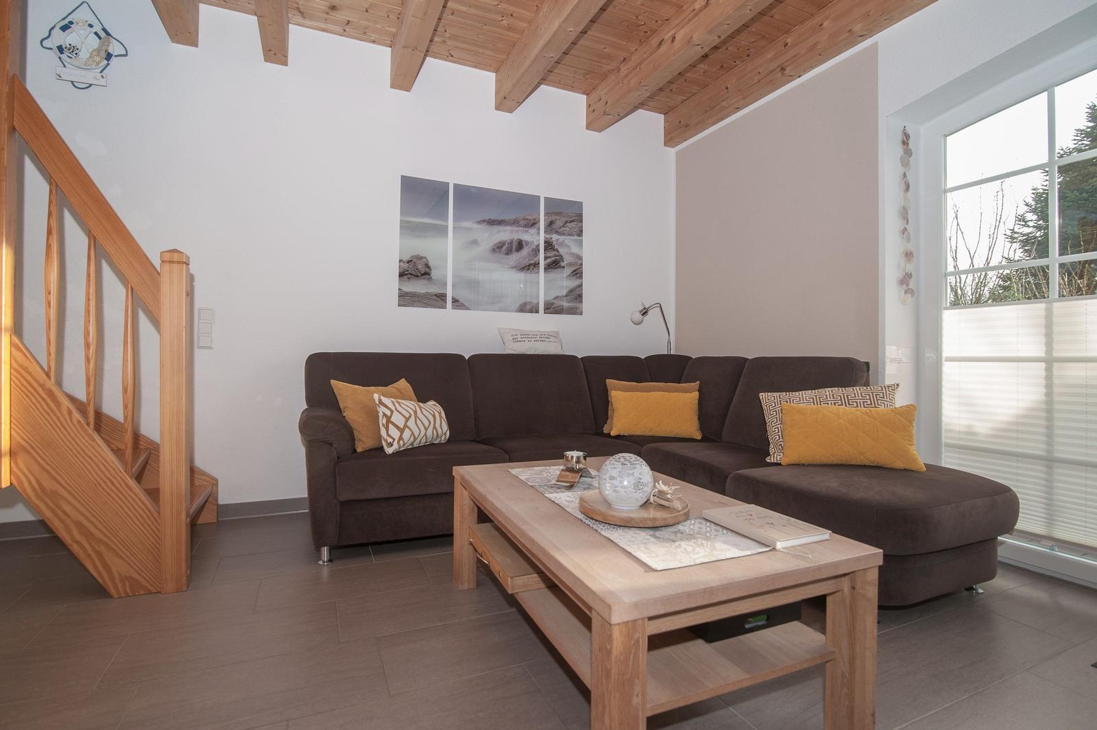 Wohnzimmer mit braunem Sofa, Holztisch und Holzdecke. Fenster mit Jalousie und Wandbild.