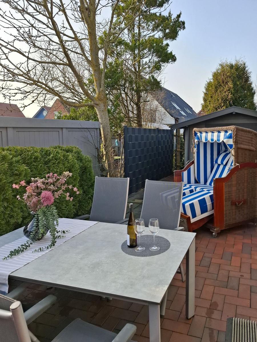 Terrasse mit Tisch, Stühlen, Strandkorb und Blumenarrangement.