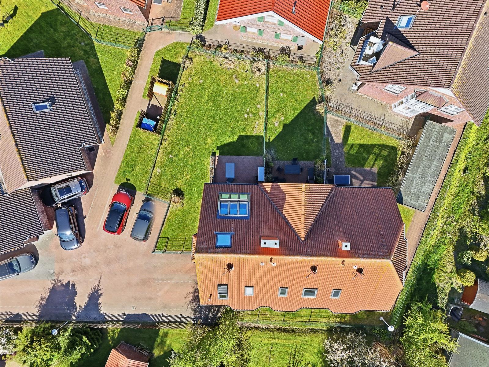 Haus mit rotem Dach, Garten und Parkplatz mit mehreren Autos.