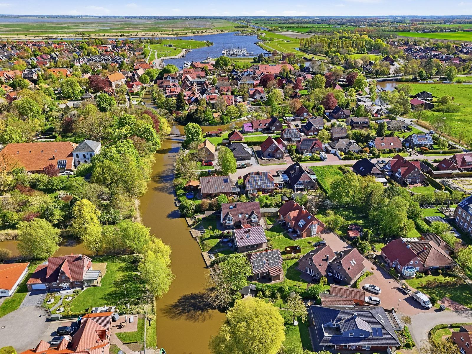 Luftbild eines Dorfes mit Häusern, Grünflächen und einem Fluss.