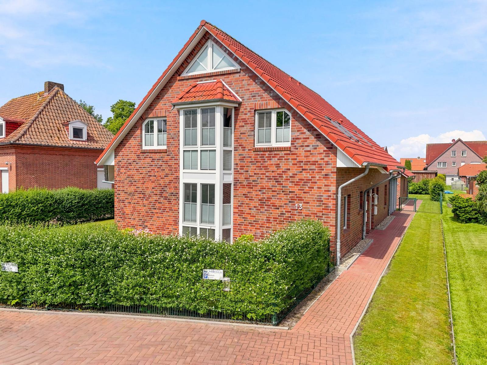 Rotes Ziegelhaus mit Dachgaube und Balkon. Vorgarten mit Hecke und gepflastertem Weg.