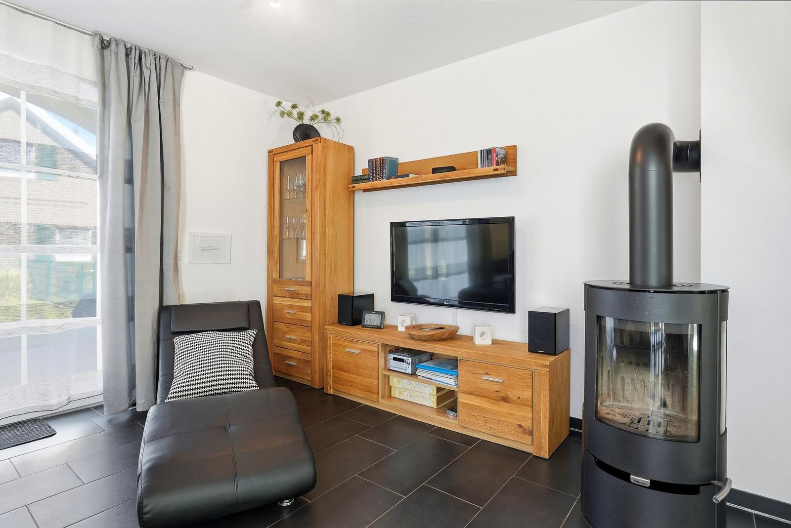 Wohnzimmer mit Holzmöbeln, Fernseher, Kaminofen und Sessel.