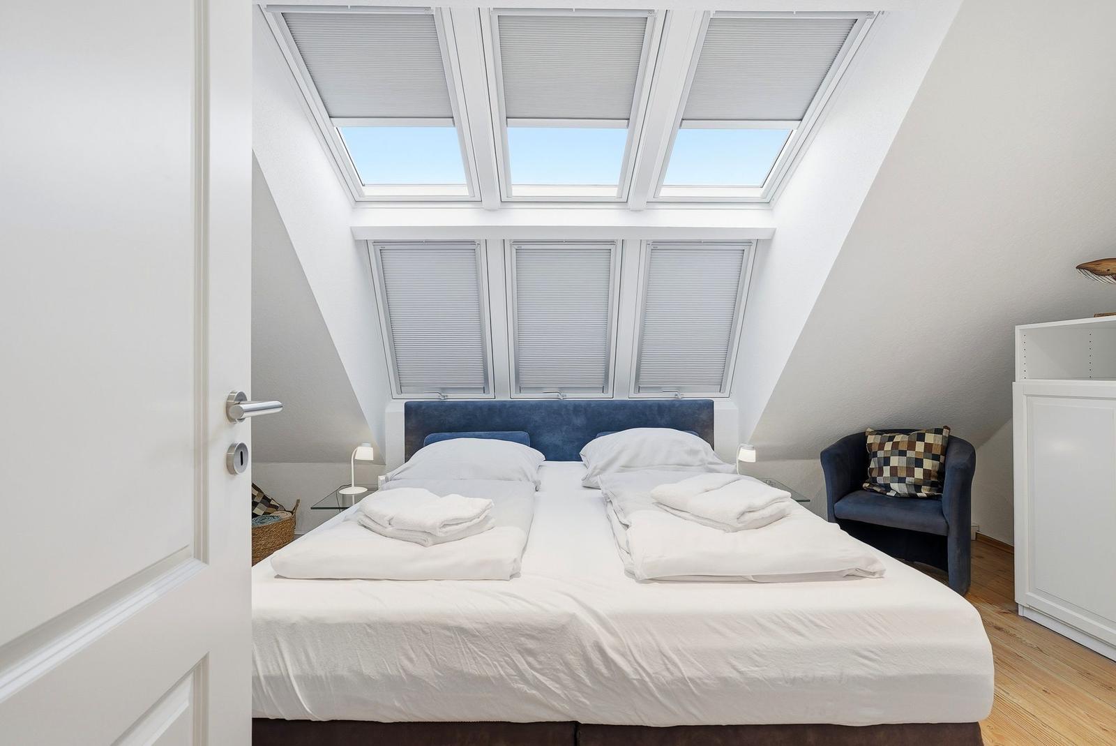 Schlafzimmer mit Doppelbett, Dachfenstern und Sitzgelegenheit.