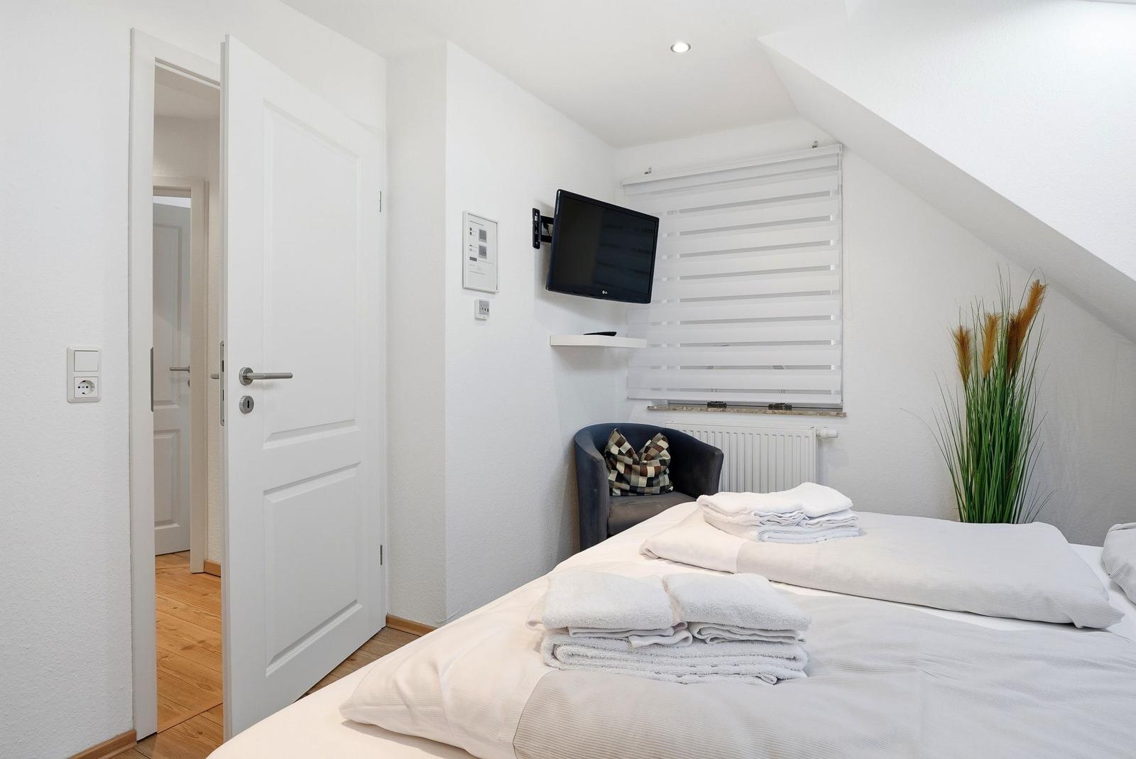 Schlafzimmer mit Bett, Fernseher und Sessel unter Dachschrägen.