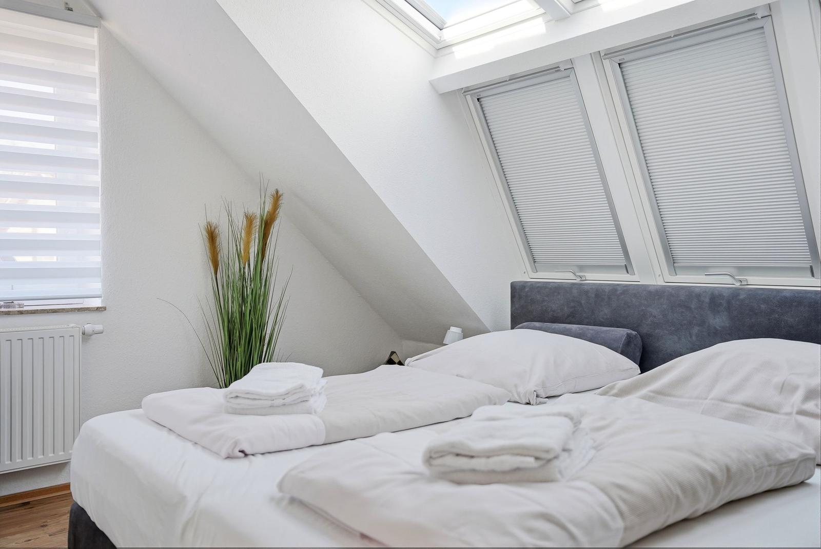 Schlafzimmer mit Dachschrägen, Dachfenster und Bett mit weißer Bettwäsche.