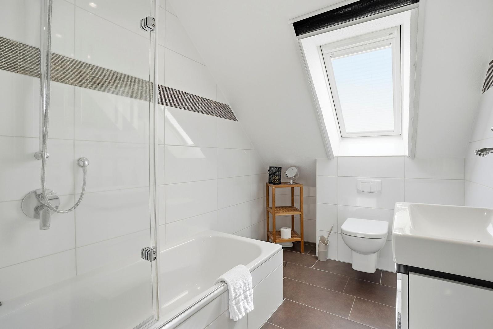 Badezimmer mit Dusche, Badewanne, Toilette und Waschbecken unter Dachschrägen.