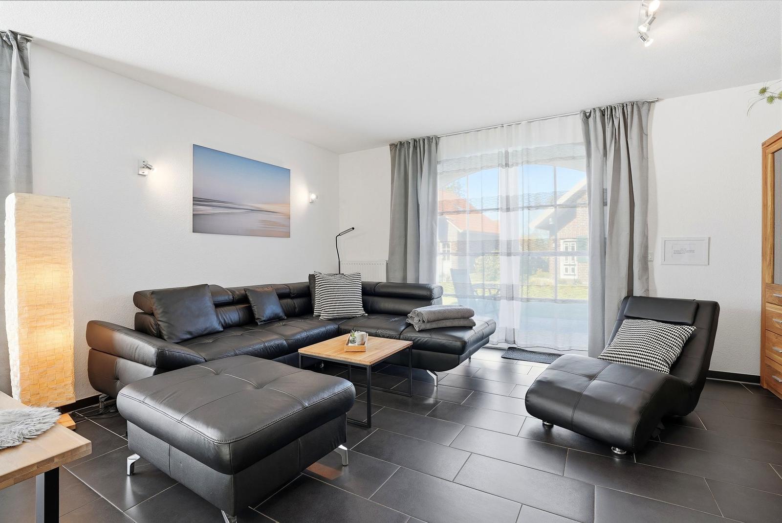 Wohnzimmer mit schwarzer Ledercouch, Holztisch und großem Fenster.