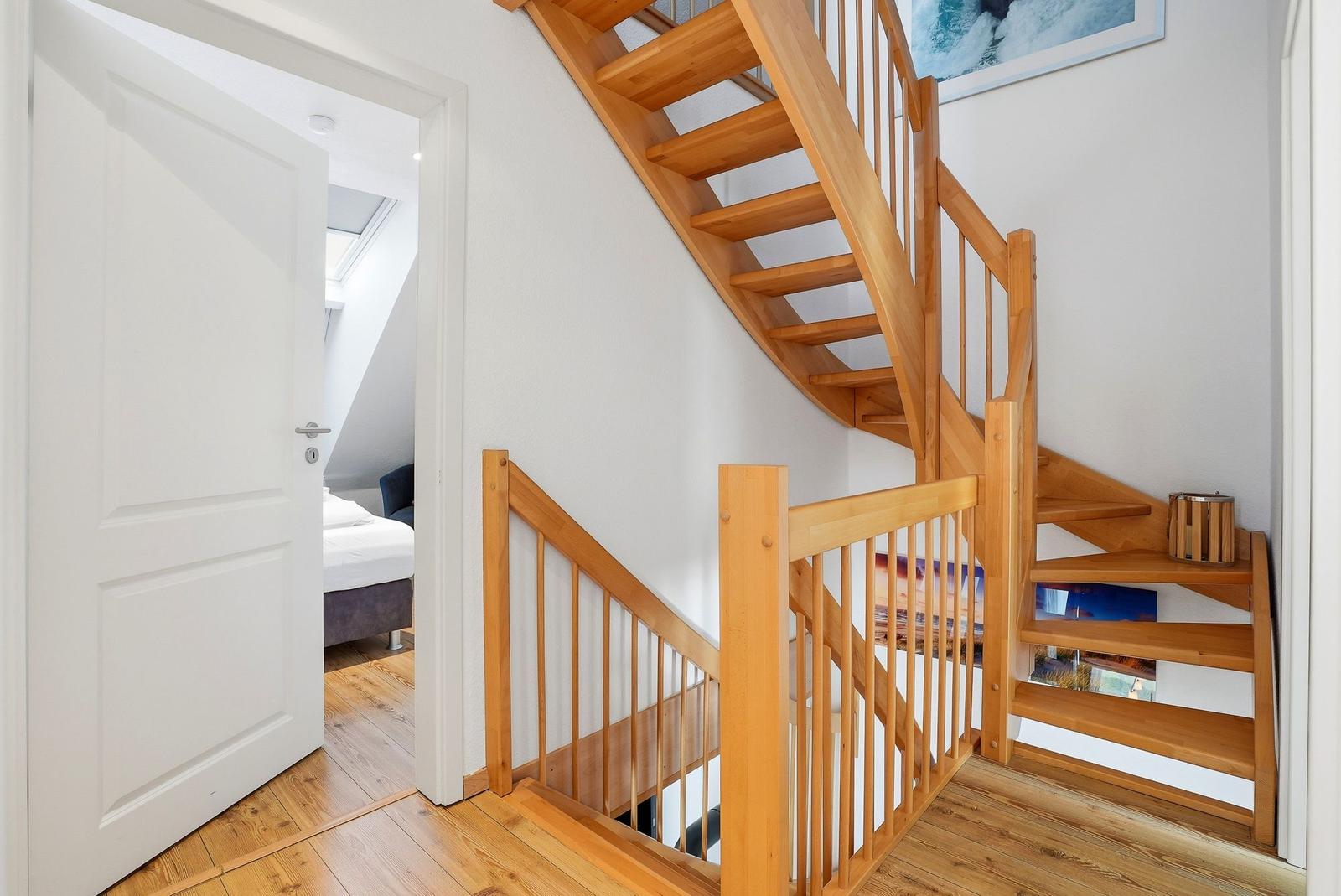 Holztreppe führt zur oberen Etage. Tür öffnet in Schlafzimmer mit Bett.