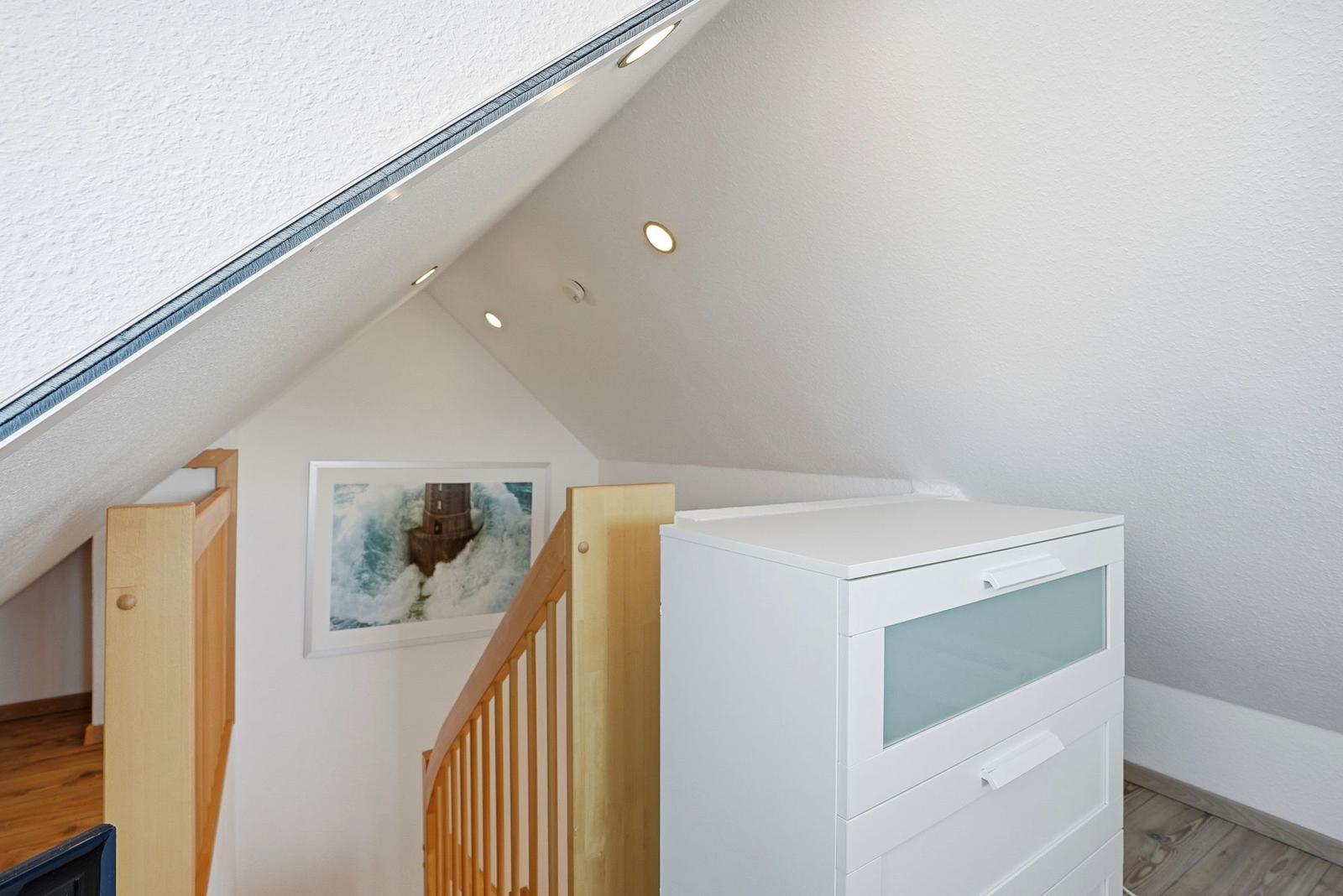 Dachgeschoss mit Holztreppenhaus, weißen Wänden und Schrank. Bild an der Wand.