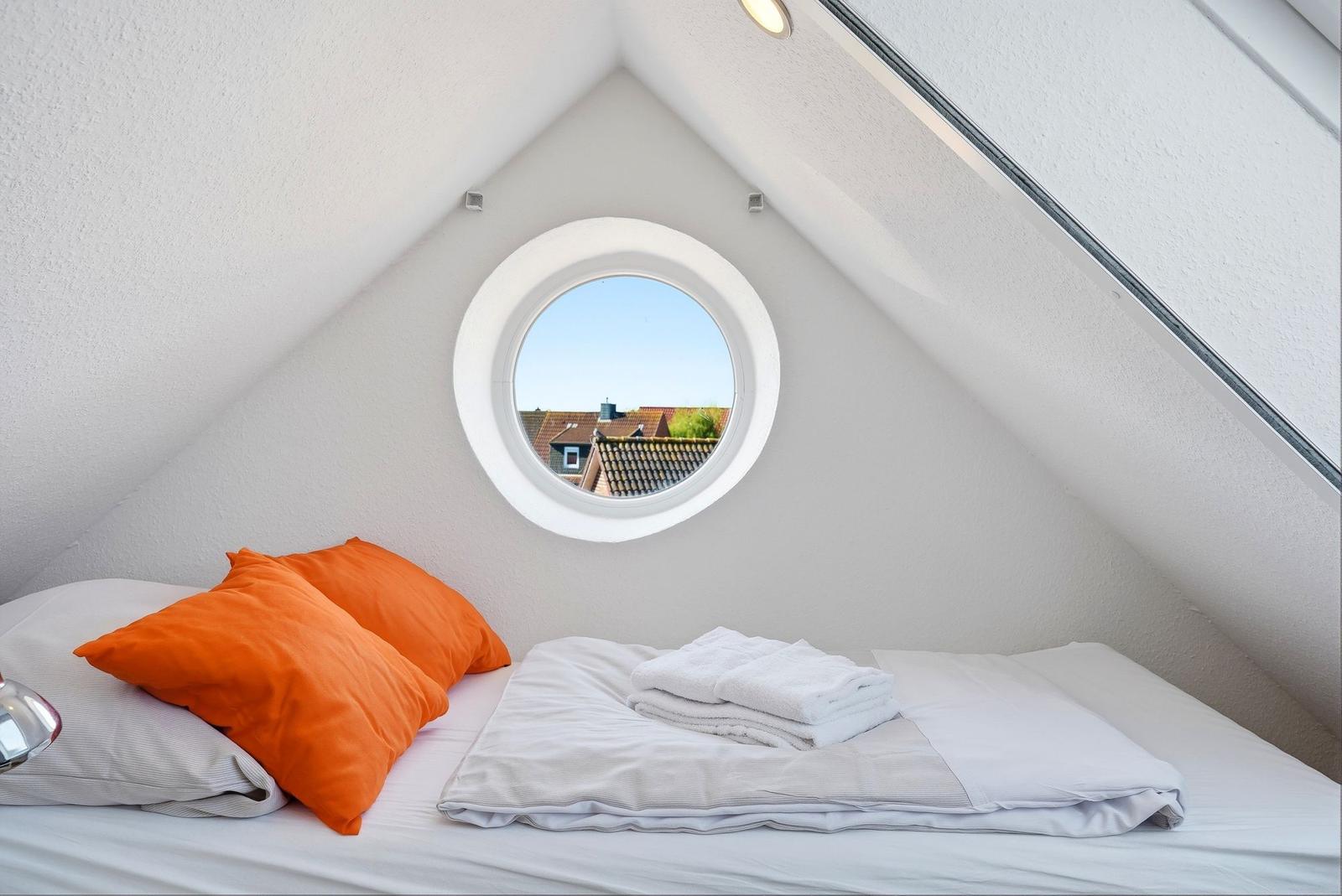 Schlafzimmer mit runden Fenster und Bett mit orangefarbenen Kissen.