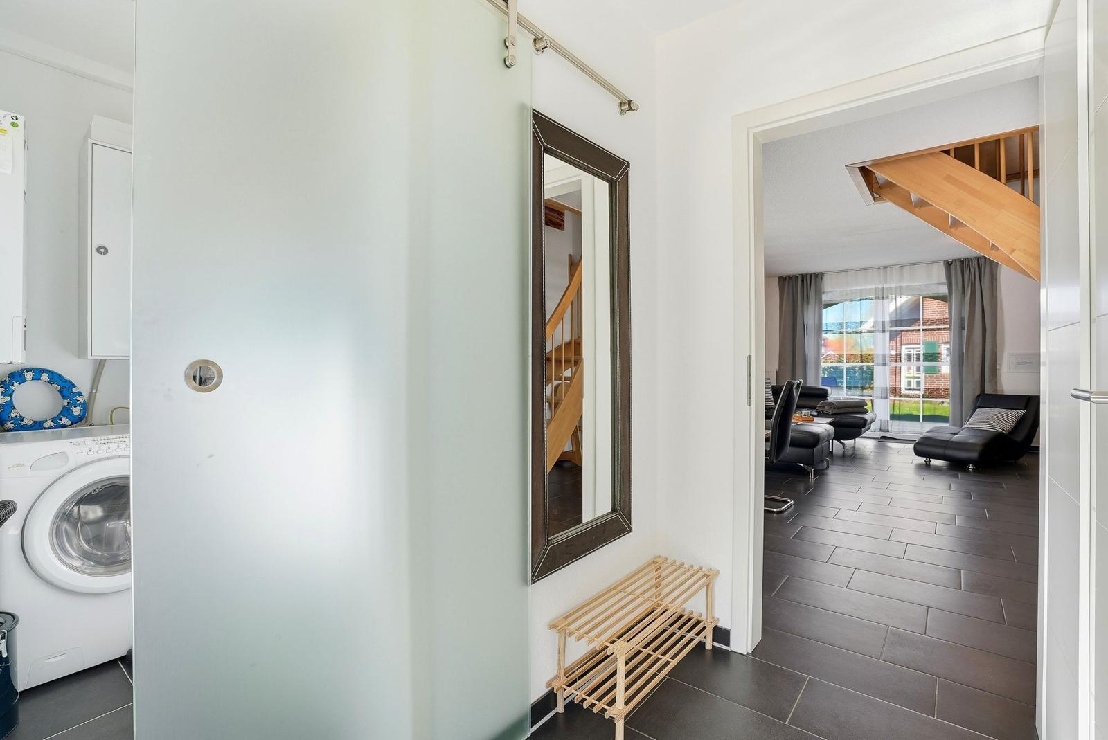 Eingangsbereich mit Spiegel, Schuhtreter und Blick in Wohnzimmer mit Holztreppe.