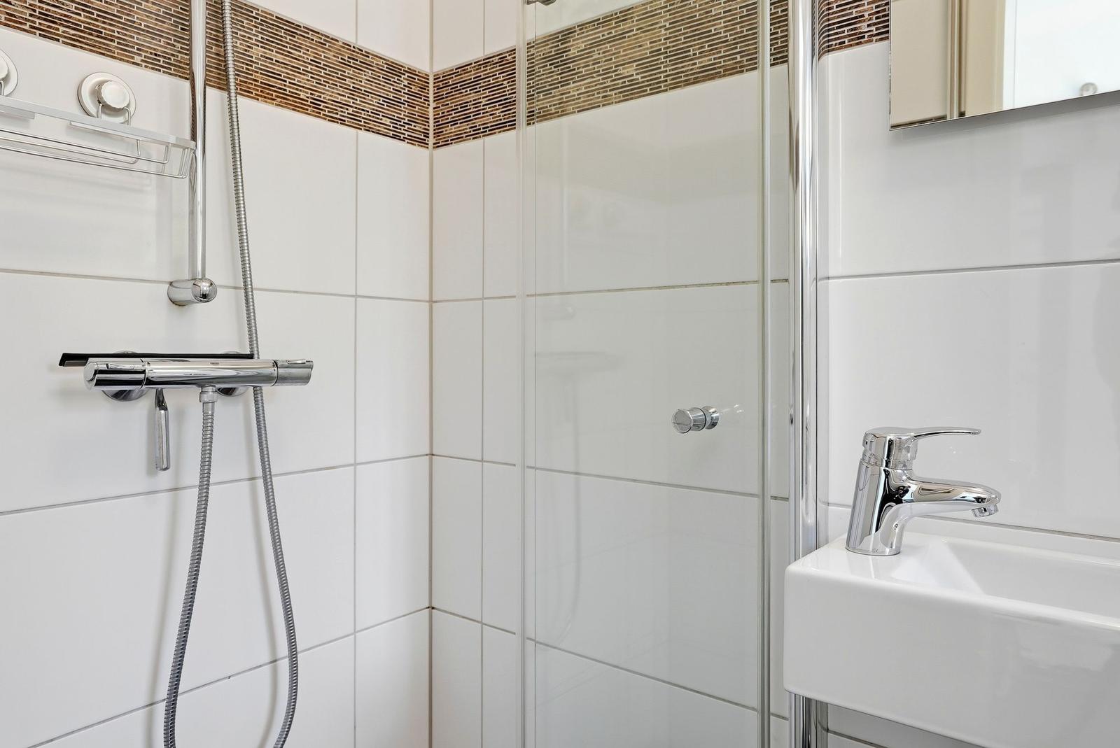 Badezimmer mit Dusche, Waschbecken und Spiegel. Weiße Fliesen und Chromarmaturen.