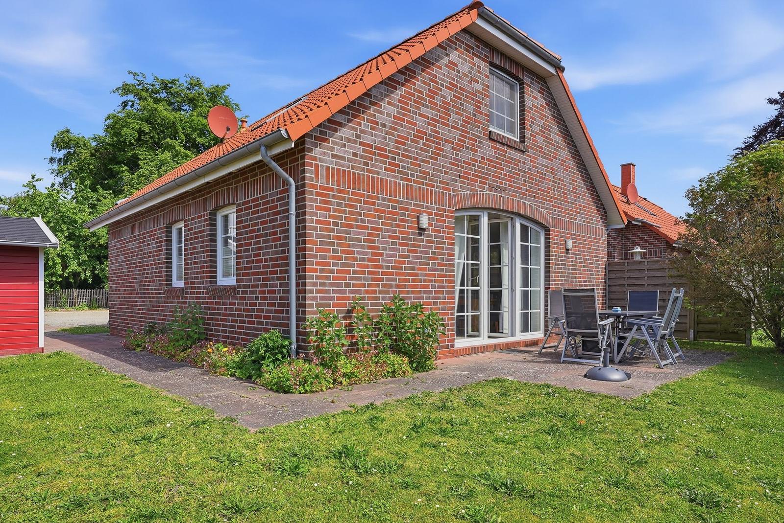 Rotes Ziegelhaus mit Terrasse und Garten. Satellitenantenne auf Dach.