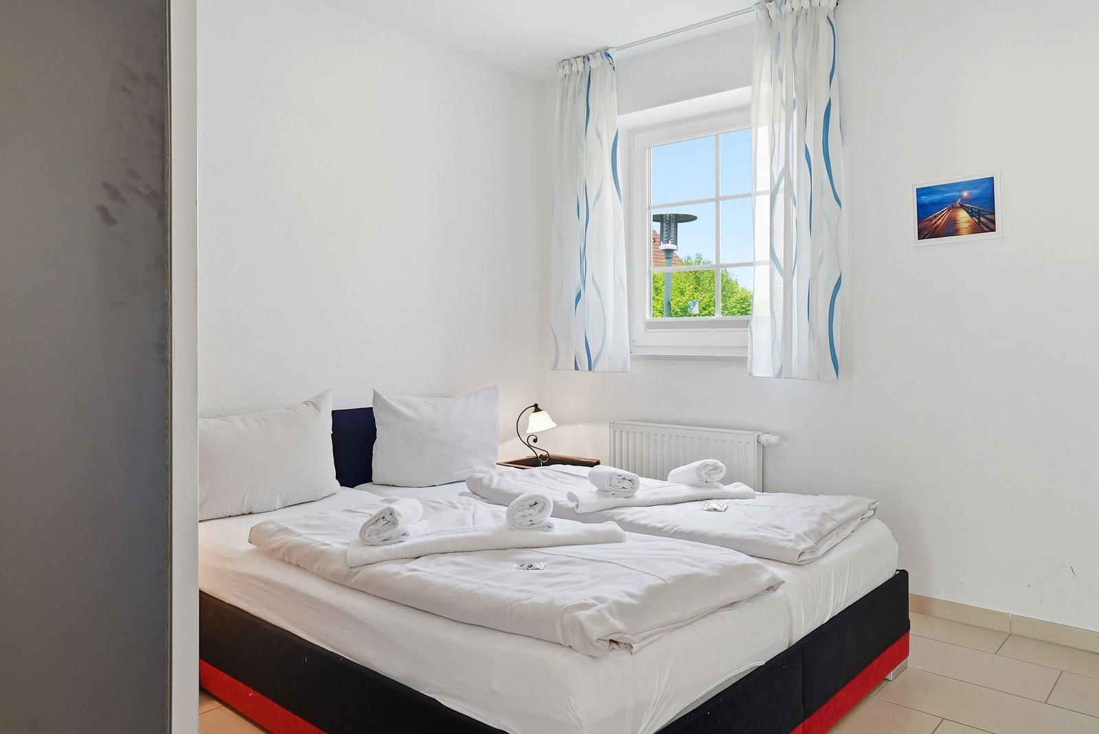 Schlafzimmer mit Doppelbett, Fenster und weißen Wänden.