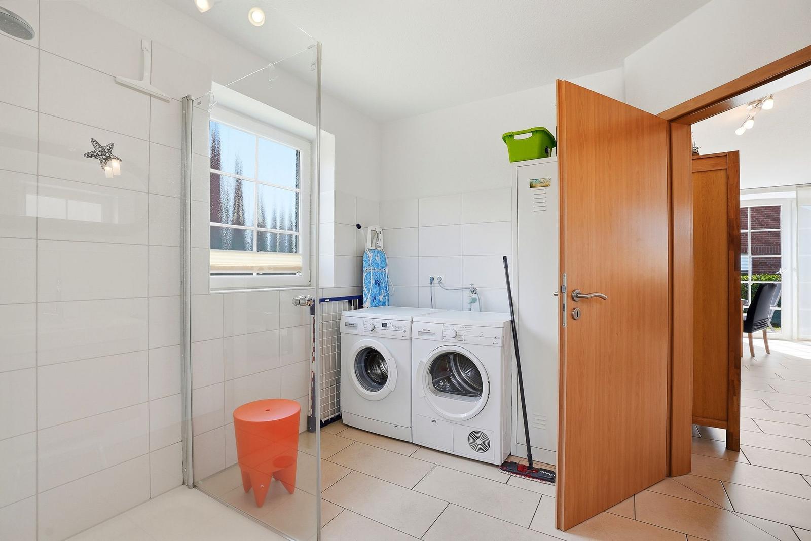 Waschraum mit Waschmaschine, Trockner und Dusche mit Glaswand.