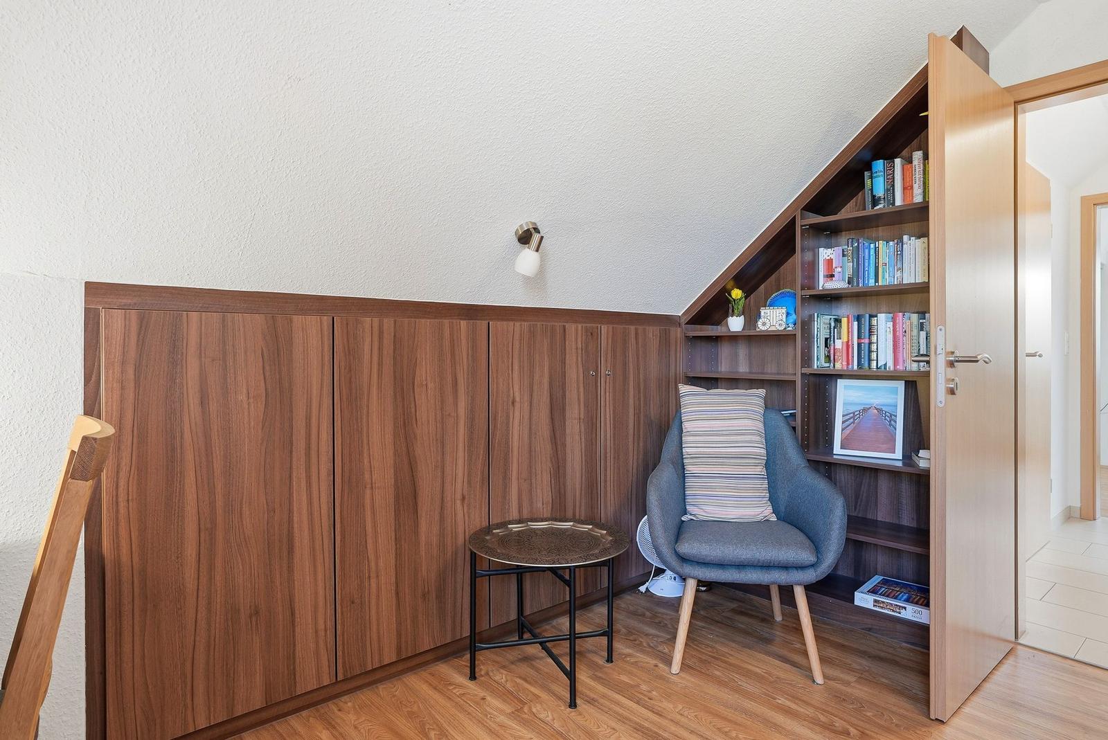 Eckzimmer mit Bücherregal, Stuhl und Tisch. Holzwand und Holzfußboden.