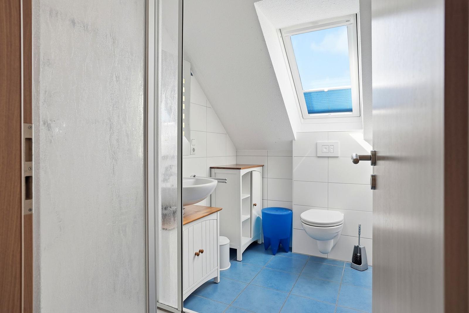 Badezimmer mit Dachfenster, blauem Boden und weißen Fliesen.