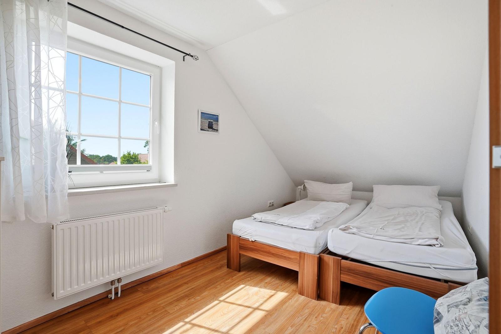 Zimmer mit zwei Betten, Holzboden und großem Fenster mit Blick nach draußen.