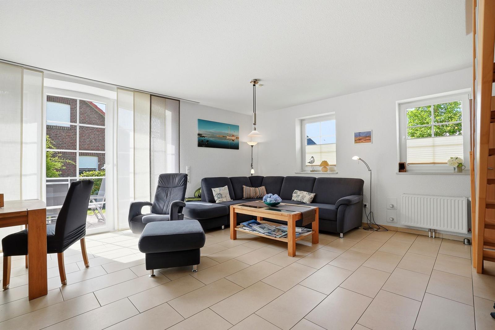 Wohnzimmer mit Sofa, Sessel und Tisch. Fenster und Glastür führen auf Balkon.