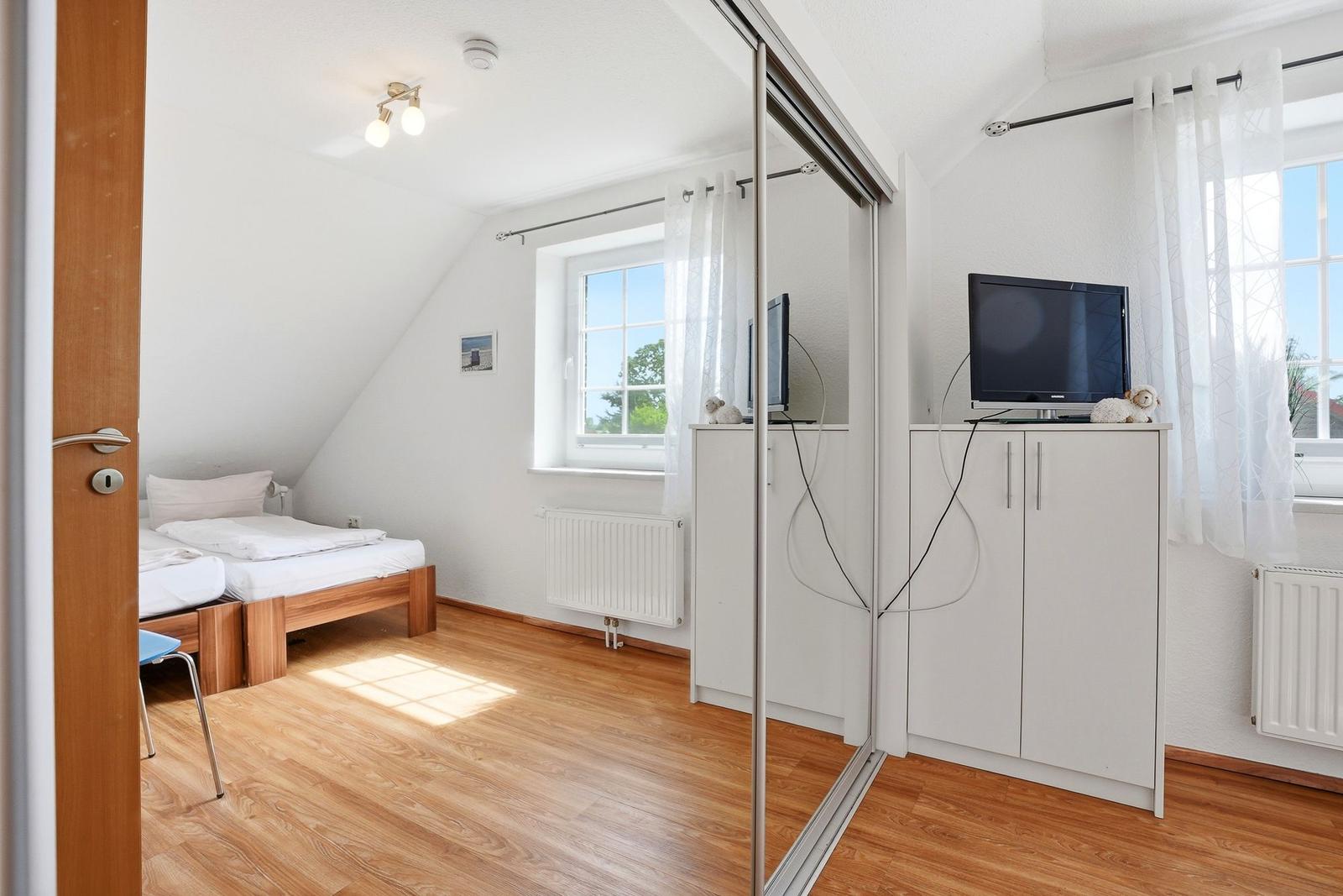 Schlafzimmer mit Dachschräge, Bett, TV und Holzboden.