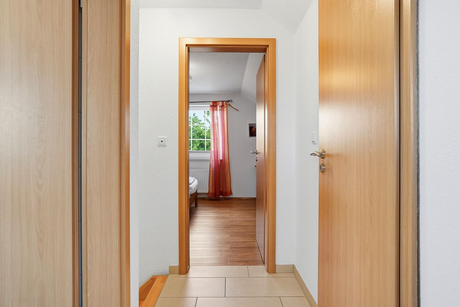 Flur mit Holztüren und Blick in ein Schlafzimmer mit Holzboden und Fenster.
