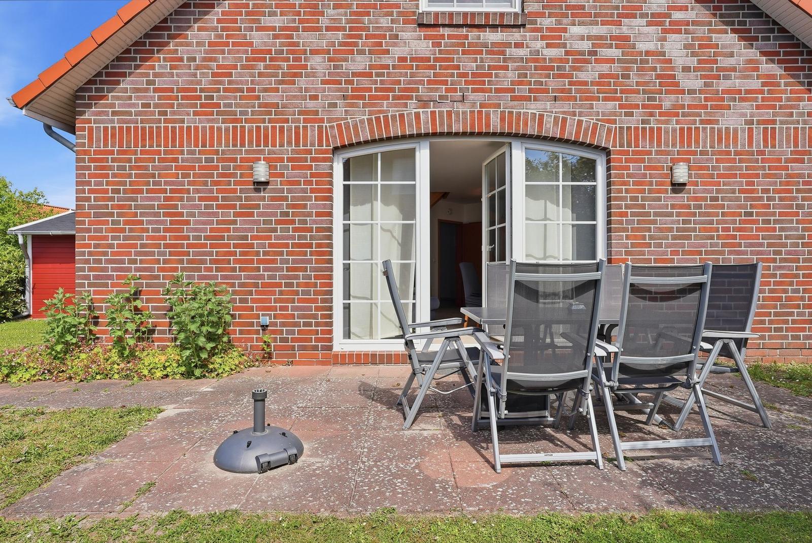 Roter Backsteinbau mit Terrasse, Gartenmöbel und Grillplatz.