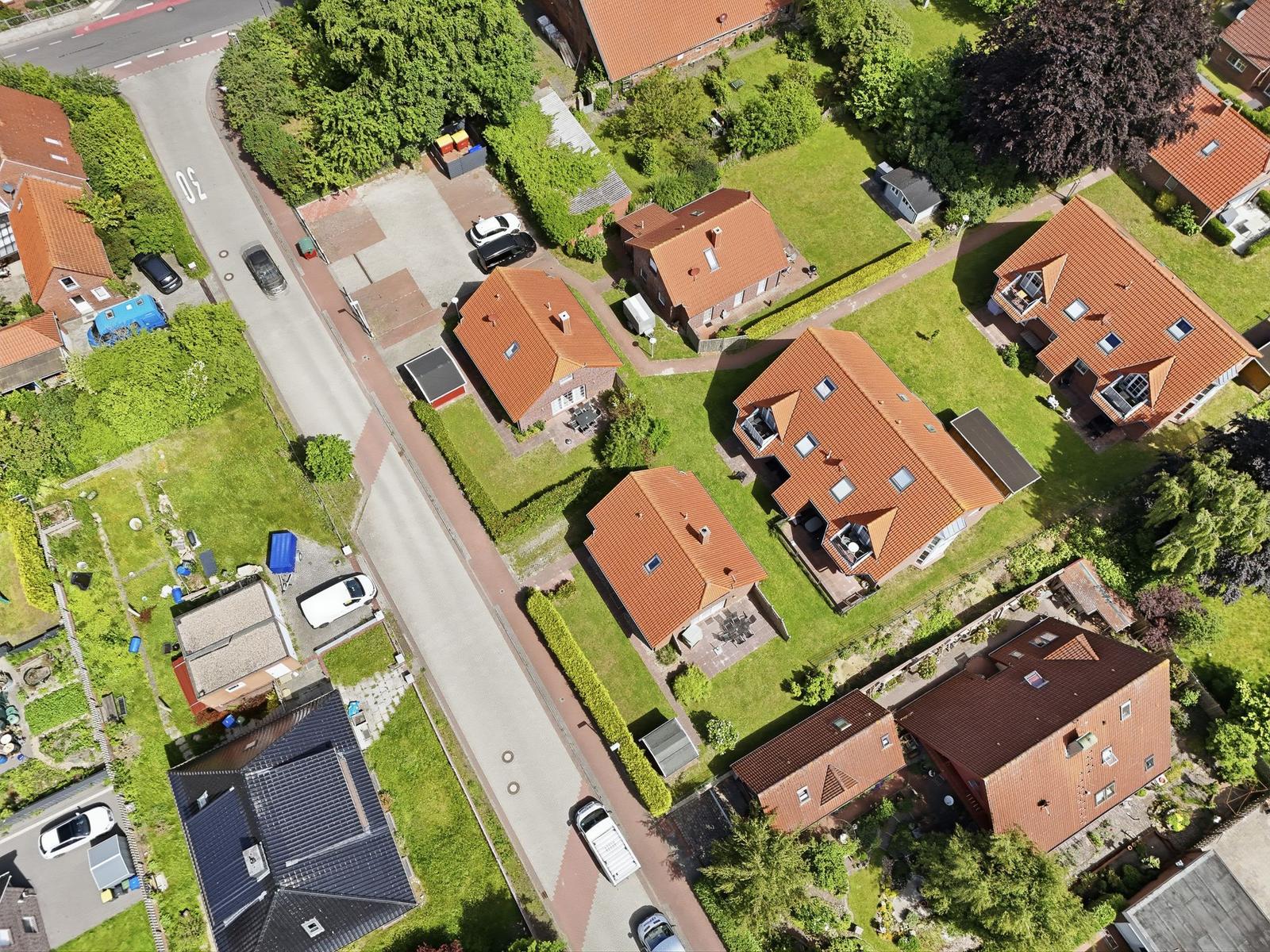 Luftbild von Häusern mit roten Dächern und grünen Gärten entlang einer Straße.