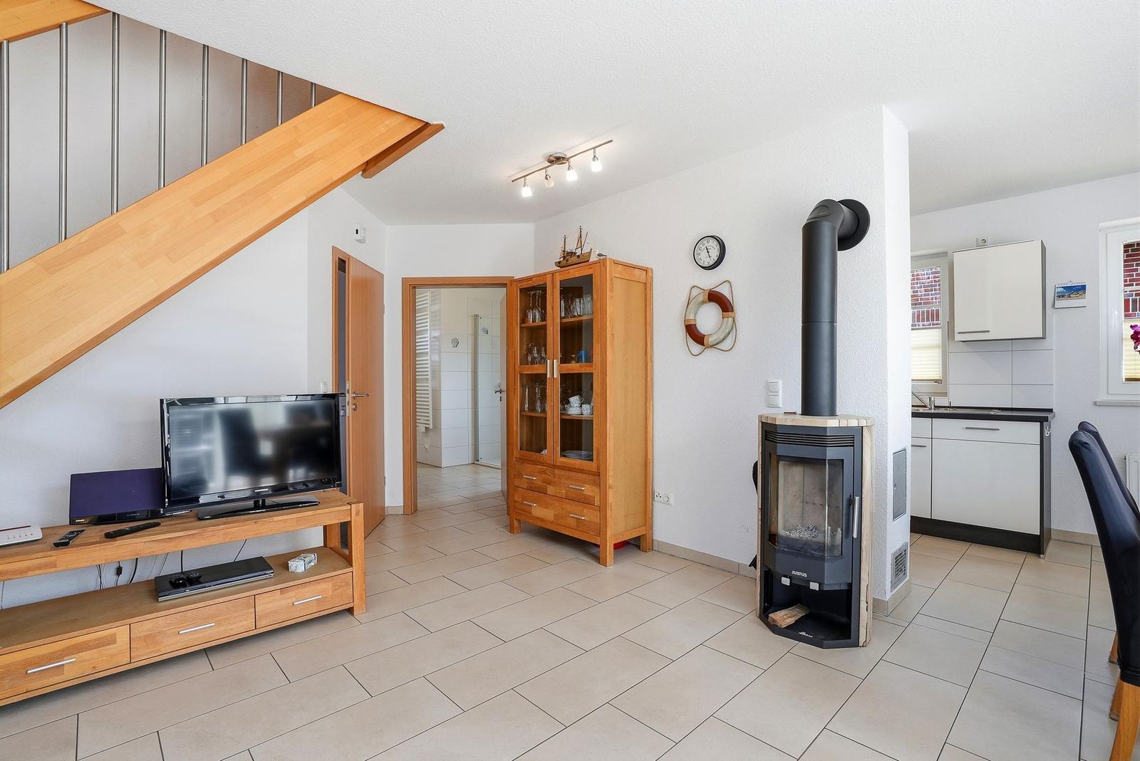 Wohnbereich mit Holztreppe, TV, Kaminofen und Küchenbereich.