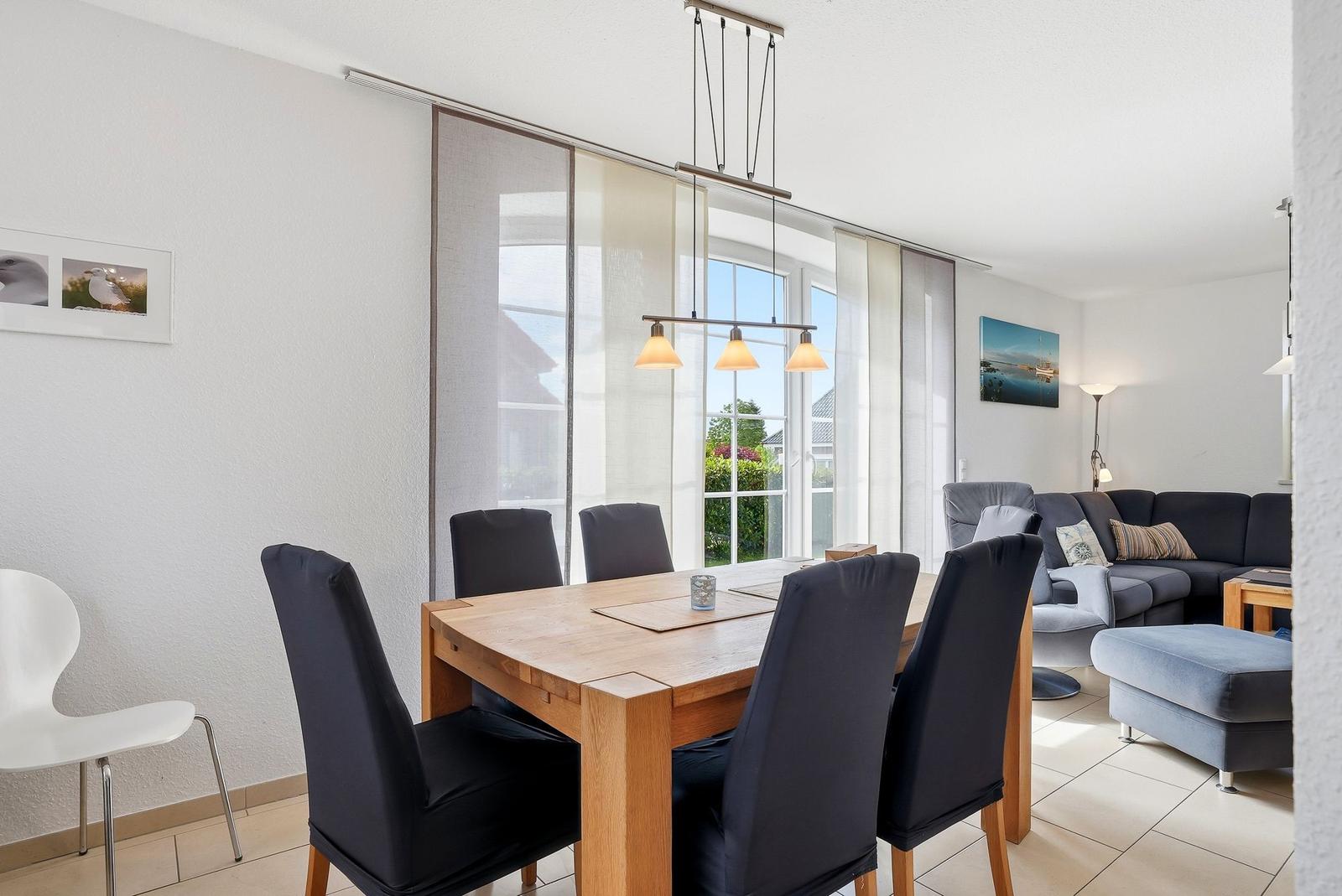 Essbereich mit Holztisch und Stühlen. Wohnzimmer mit Sofa und Fenster.