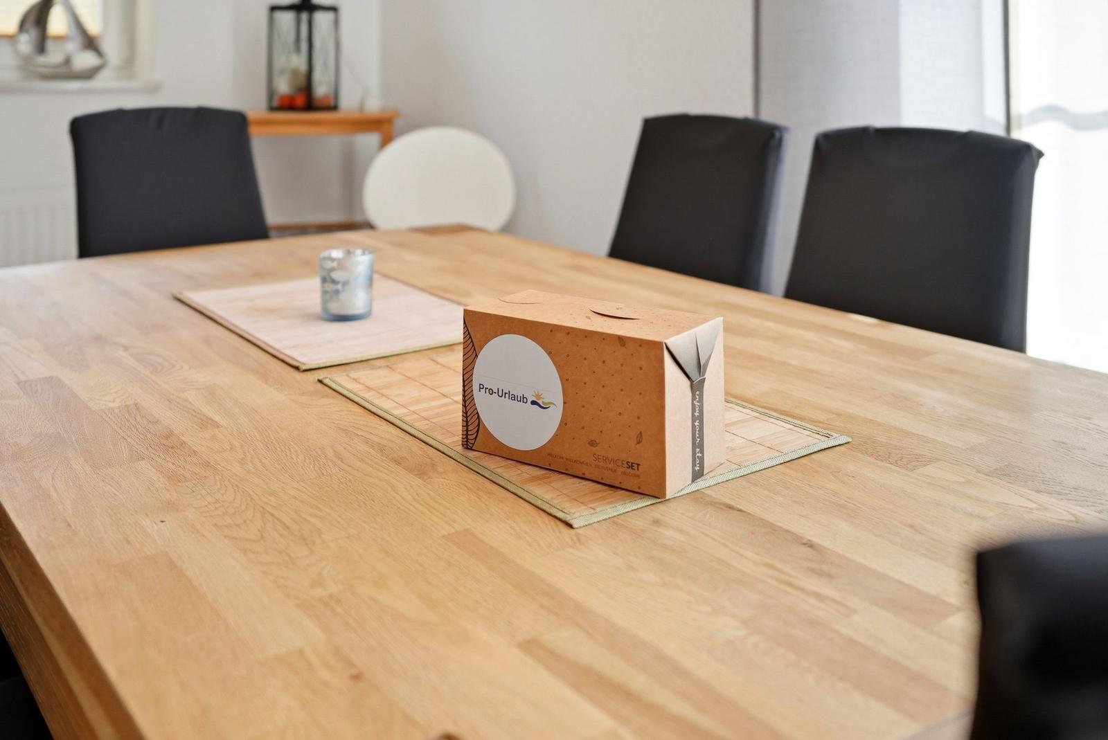 Holztisch mit Stühlen und Servicebox auf Platzteppichen.