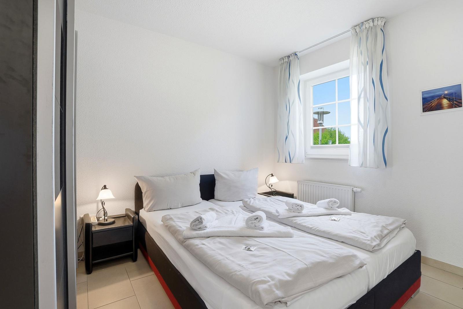 Ein Schlafzimmer mit Doppelbett, zwei Nachttischen und einem Fenster mit Vorhängen.