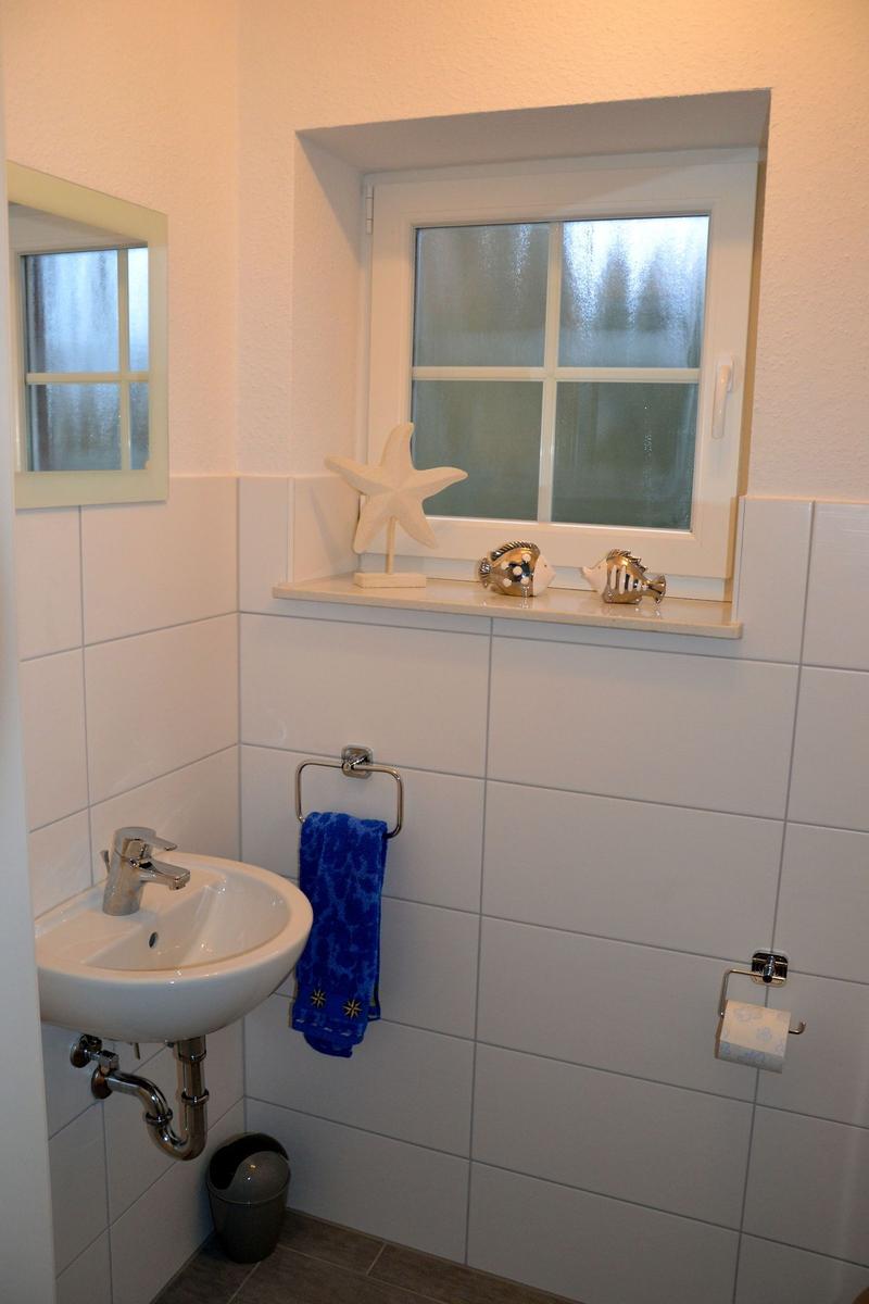 Badezimmer mit Waschbecken, Fenster und Handtuchhalter. Auf dem Sims stehen dekorative Fische und eine Seesternfigur.