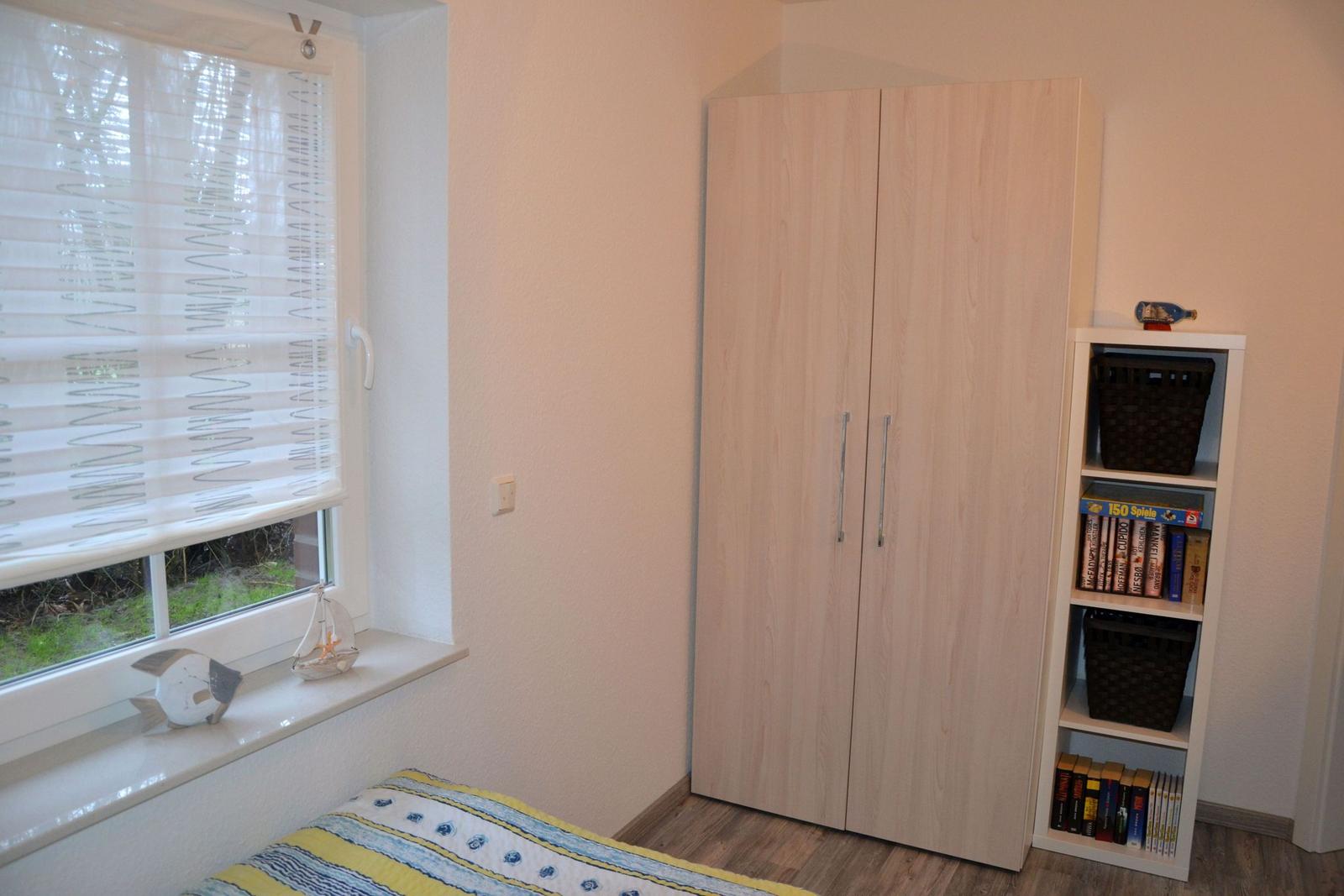 Schlafzimmer mit Kleiderschrank, Bücherregal und Fenster mit Jalousie.