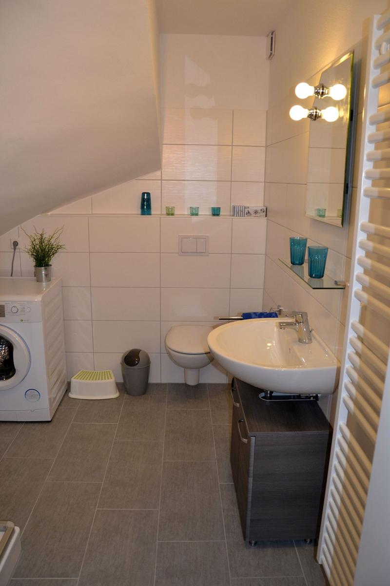 Badezimmer mit Waschmaschine, Toilette und Spiegel mit Beleuchtung.