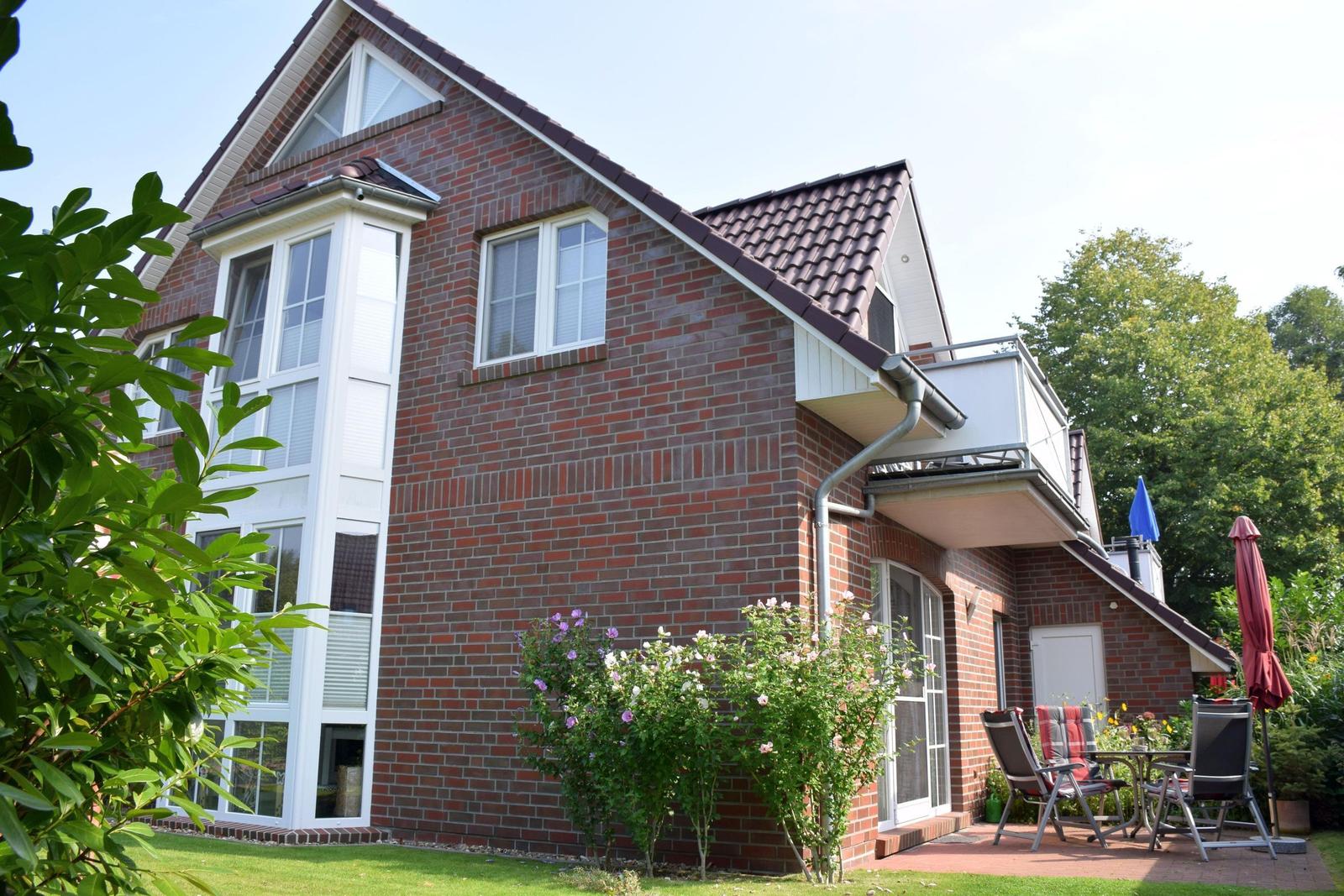 Zweistöckiges Haus mit Balkon, Garten und Terrasse mit Sitzgelegenheiten.