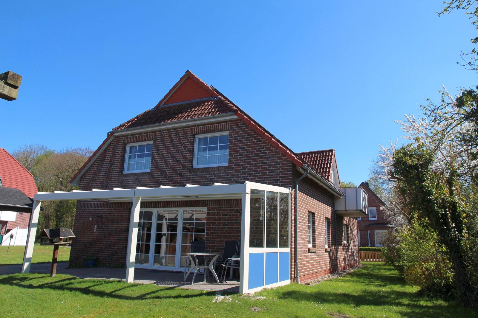 Red tiled roof, white veranda with table and chairs, green lawn and trees in the background.