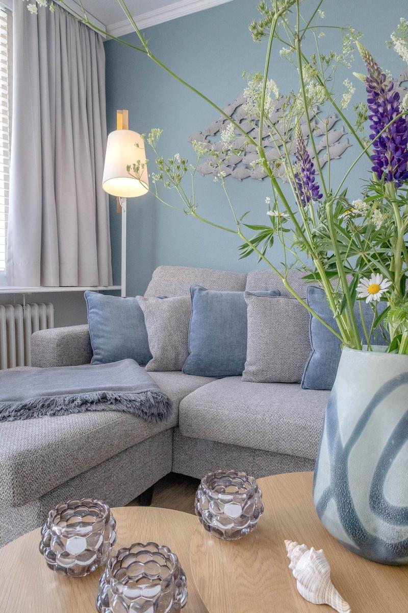 Ein Wohnzimmer mit grauem Sofa, Blumen und einer Stehlampe.
