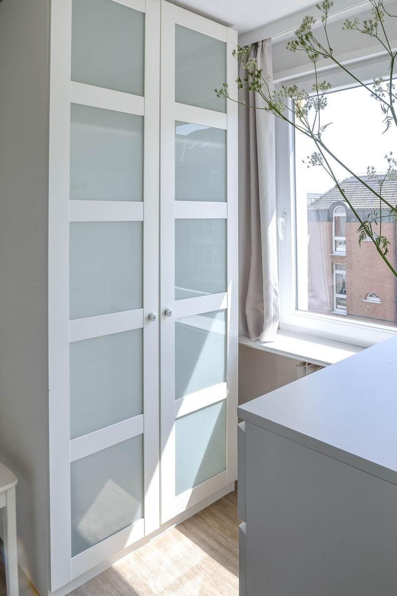 Weißer Schrank mit getöntem Glas steht neben einem Fenster mit Blick auf Gebäude.