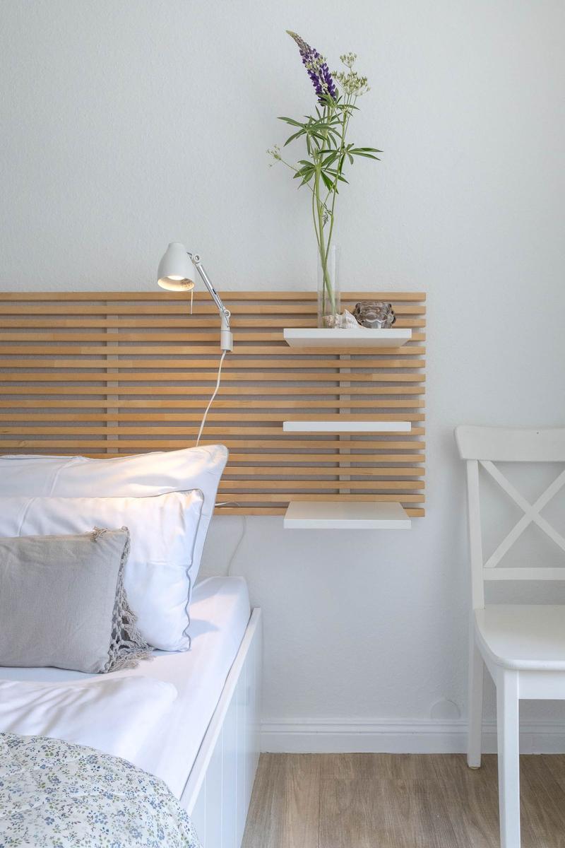 Schlafzimmer mit Bett, Holz-Kopfteil und weißer Stuhlecke