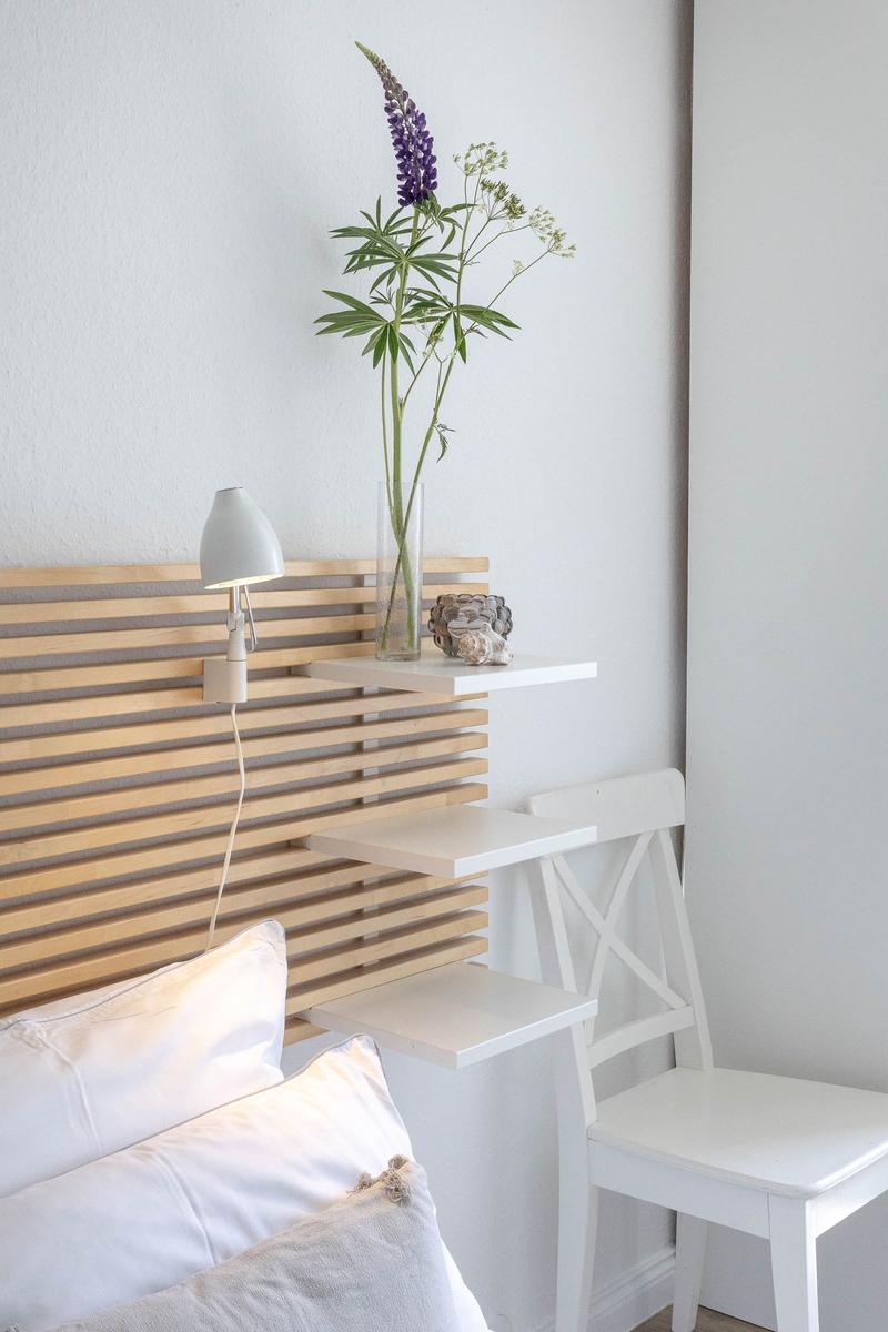 Schlafzimmer mit Holzkopfteil, weißen Kissen und Blumen im Glas.
