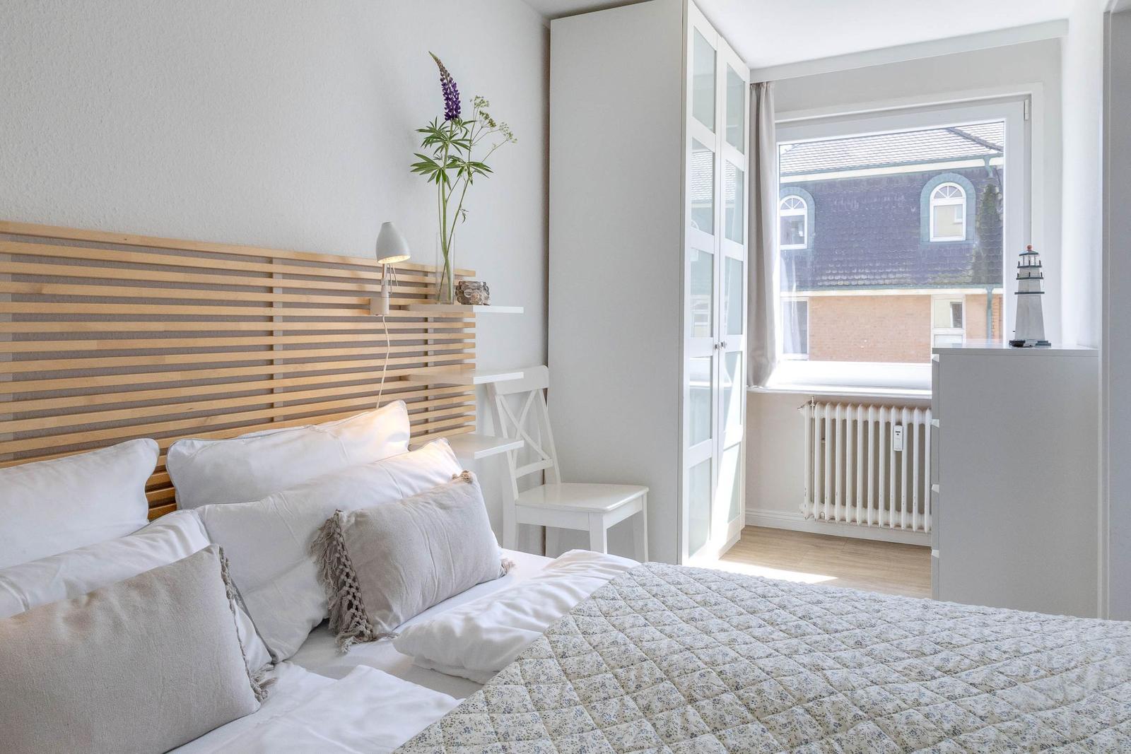 Schlafzimmer mit Bett, Holzkopfteil und Fensterblick auf Haus