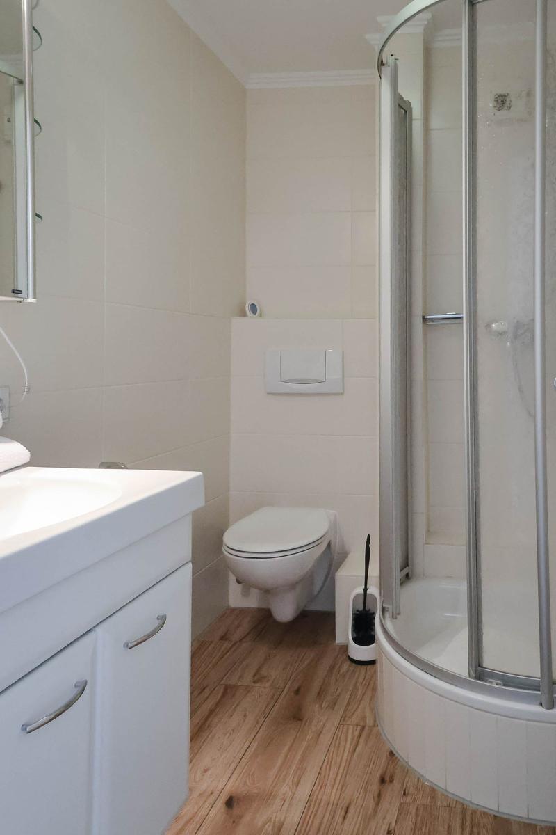Badezimmer mit Dusche, Toilette und Waschbecken auf Holzboden.