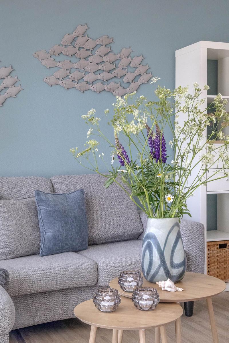 Grauer Sofa mit Kissen, Blumen in Vase, Wanddekoration mit Fischen.