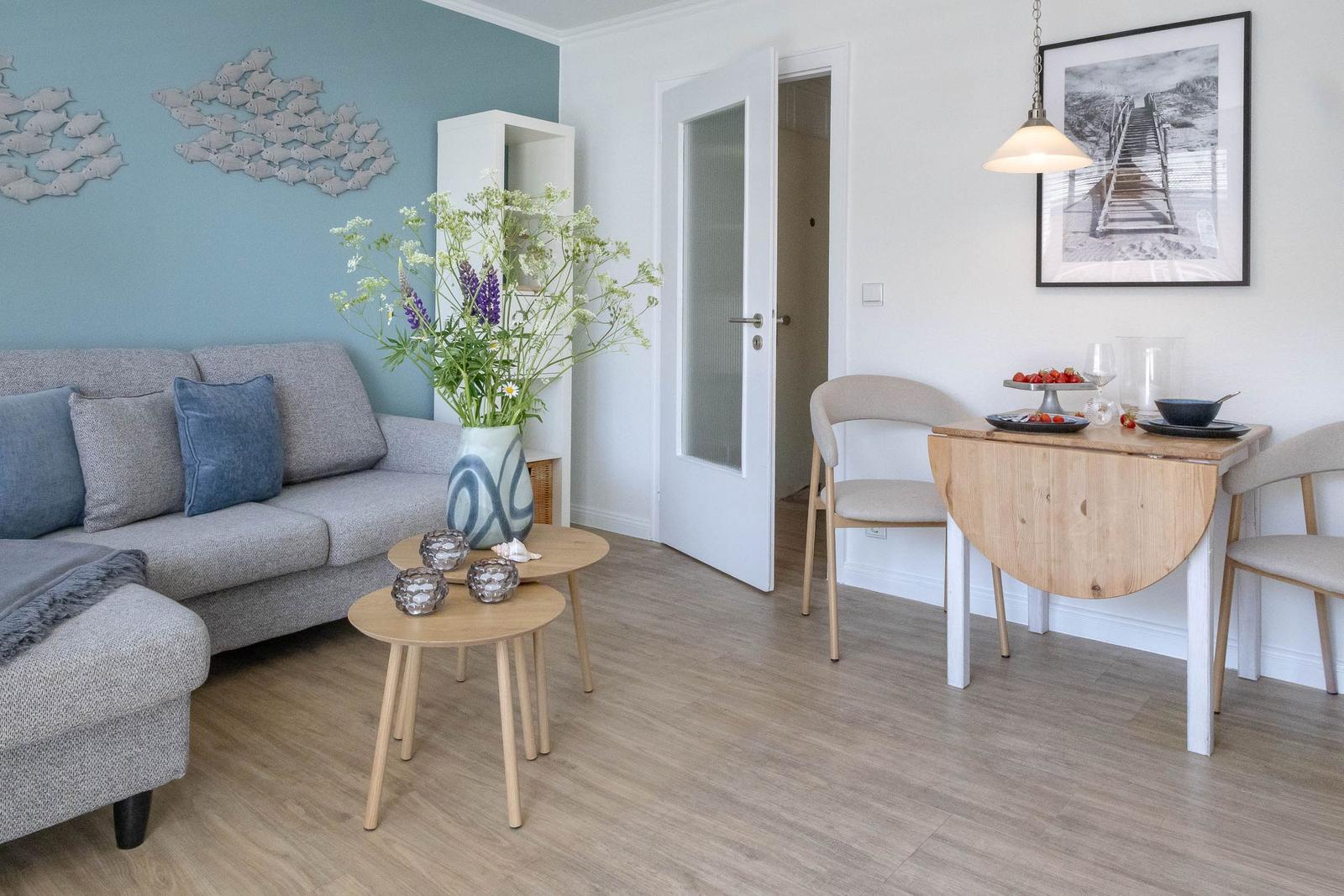 Wohn- und Essbereich mit Sofa, Tischen und Stühlen. Wanddekoration und Blumen.